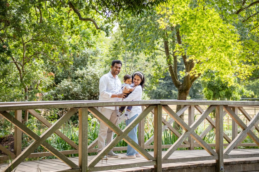 Family of three in a park by a bridge, looking at the ducks in the river