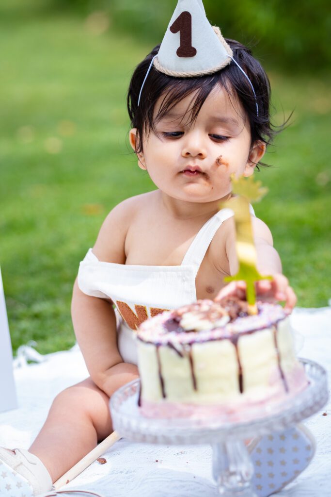 Little baby boy's first birthday photoshoot in a park, cake smash on a picnic, birthday decoration, balloons