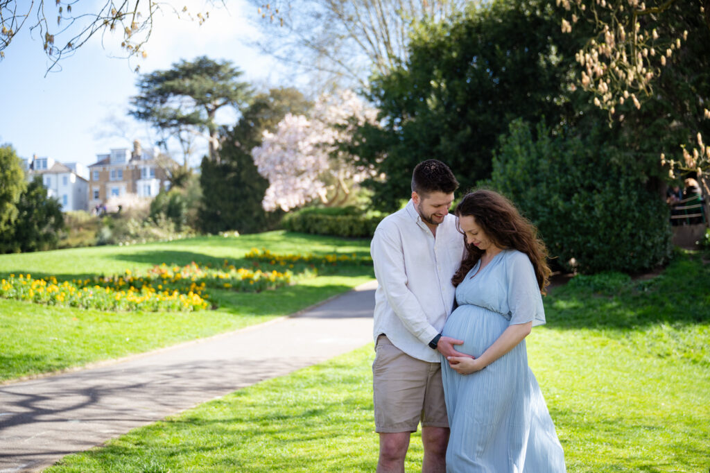 A pregnant couple enjoying a stroll in Richmond Terrace Gardens, with trees and flowers in the background.
