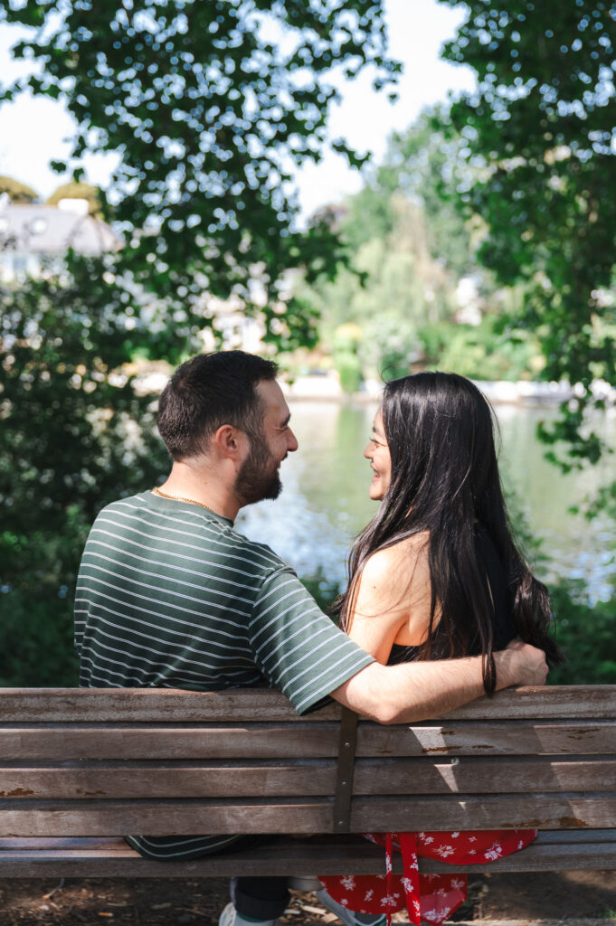 Couple sitting on a bench, looking at each other, love couple photoshoot, photo session by river Thames in Canbury gardens 